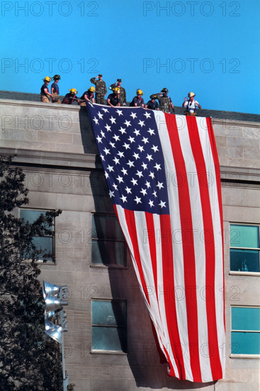 Firefighters hanging large American flag from roof of Pentagon near crash site of American Airlines