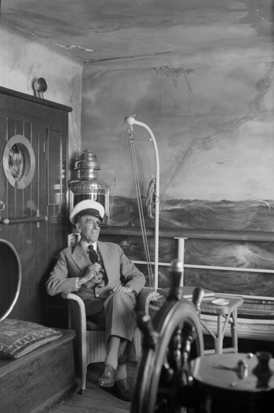 A man in a sailor's cap and eyepatch sits in a reconstructed ship's cabin, c1945-c1965
