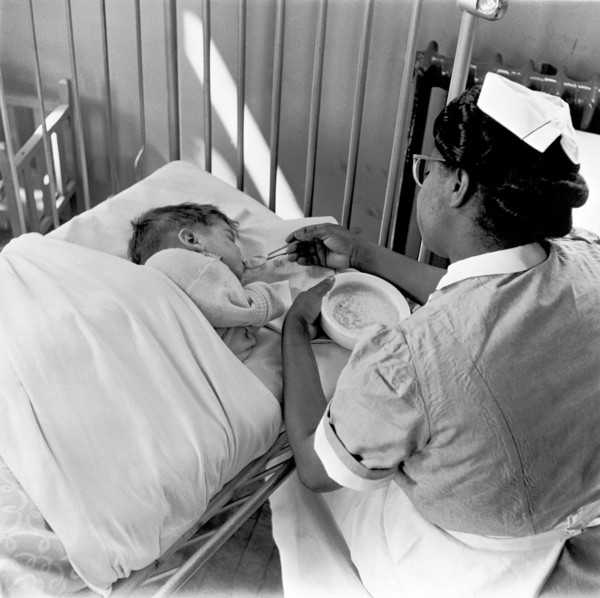 Nurse feeding a child, London, (1960s?). Creator: Henry Grant.