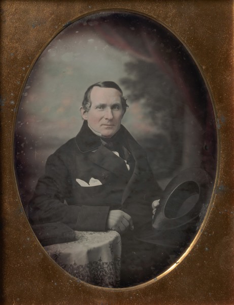 Man Wearing Coat and Gloves, Holding Hat, Seated in Front of Painted Outdoor Backdrop, 1840s.