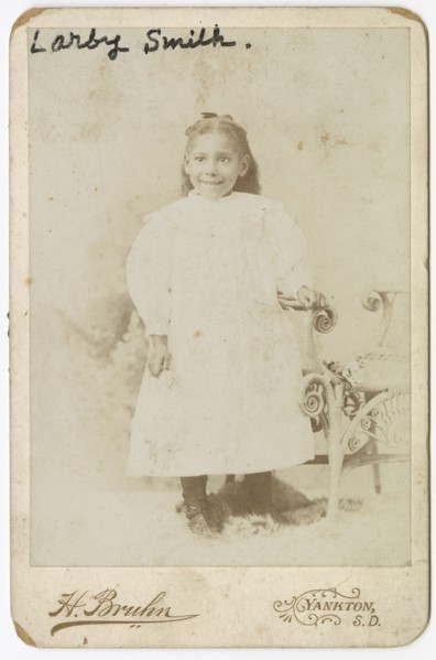 Photograph of Larby Smith standing next to a wicker chair., late 19th century. Creator: Henry Bruhn.
