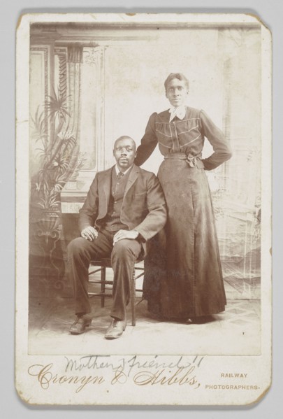 Photograph of a man sitting down with a woman standing next to him, 1880s - 1900. Creator: Cronyn & Hibbs.