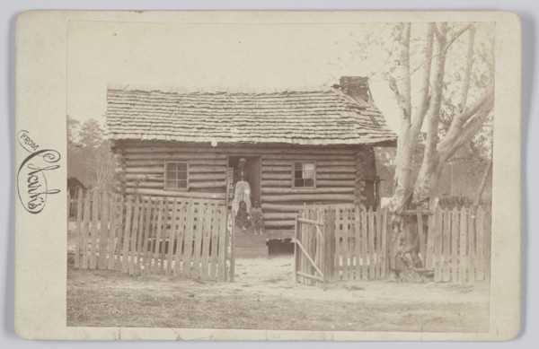 Albumen print of a woman and two children in front of a log house in Georgia, 1880s. Creator: H. S. Clark.