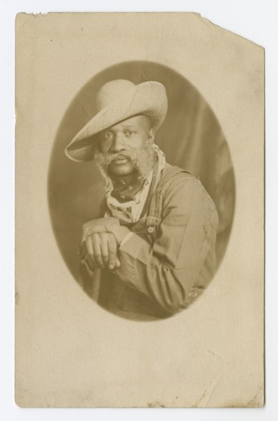 Photographic postcard portrait of a man wearing a hat and overalls, early 20th century. Creator: Unknown.