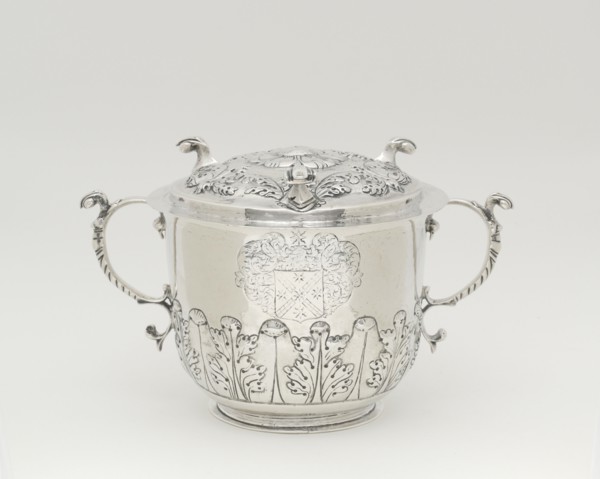 Two-Handled Covered Cup, 1698/1720. Silver cup with lid, two handles with leaf designs, used to serve syllabub, a sweetened or flavoured wine, cider, beer, or ale into which milk was whipped. Scroll-l...