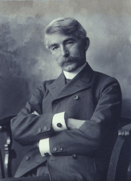 Portrait of man wearing a pinstripe suit seated with his arms crossed, c1900.