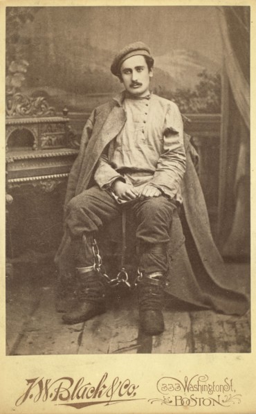 Full-length portrait of a man in convict clothing and leg irons, seated..., between 1880 and 1886. Creator: Unknown.