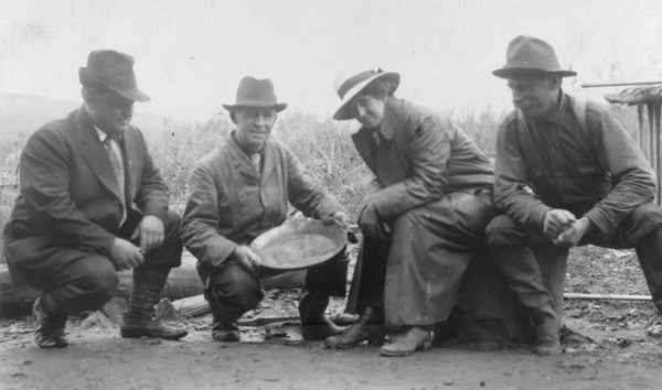 Group portrait of a woman and three men, crouched outside, smiling; one..., between c1900 and 1916. Creator: Unknown.