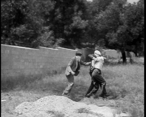Two Male American Civilians Covering Their Faces with Handkerchiefs Carrying a Male American...1930. Creator: British Pathe Ltd.