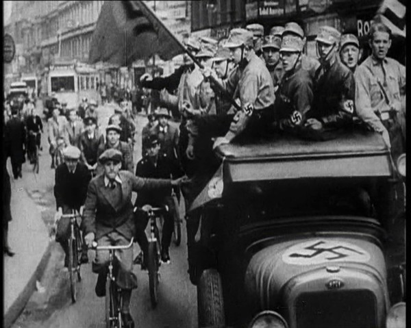 Group of Men in Nazi Uniform Driving Down the Road as Civilians Watch, 1933. Creator: British Pathe Ltd.