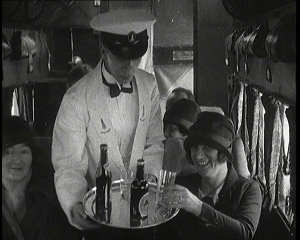 A Male Waiter Serves Smiling and Laughing Passengers Drinks  Inside an Aircraft, 1920s. Creator: British Pathe Ltd.