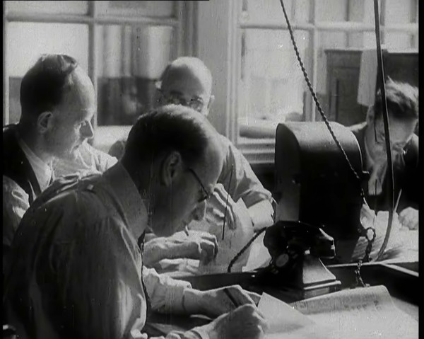 Four Male British Journalists Sitting Around a Table Covered in Papers and Writing, 1939. Creator: British Pathe Ltd.