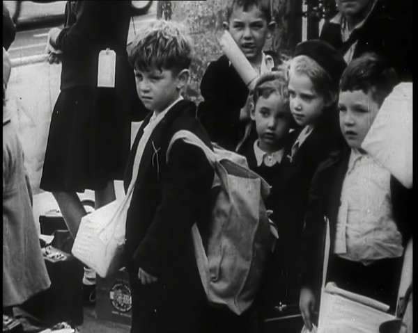 British Child Evacuees Standing on a Pavement With Bags and Boxes as Adults are Standing..., 1939. Creator: British Pathe Ltd.