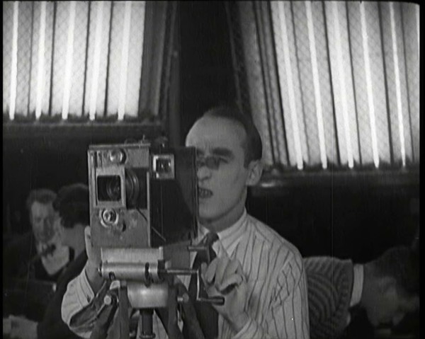 A Male Cameraman Films a Scene Whilst Lights Illuminate Behind Him, 1920s. Creator: British Pathe Ltd.