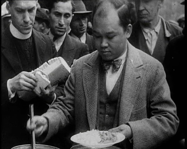 Man Serving Meals For Group of People from the Street Kitchen, 1932. Creator: British Pathe Ltd.