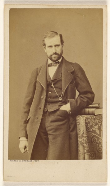Unidentified well-dressed bearded man standing, elbow on books on a table, 1865-1870. Creator: Bayard & Bertall.