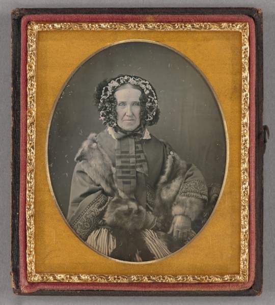 Portrait of an elderly woman wearing a hat, fur coat and gloves, seated, about 1855. Creator: Unknown.