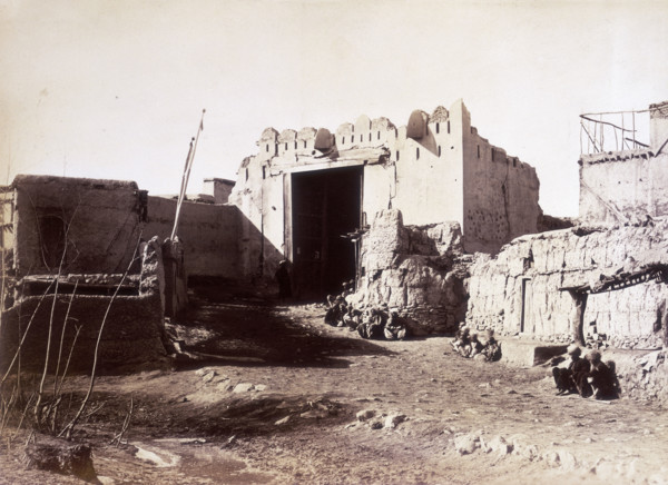 Lahore Gate, Kabul, Afghanistan, c1879. Small groups of people sit along the wall. A dirt track