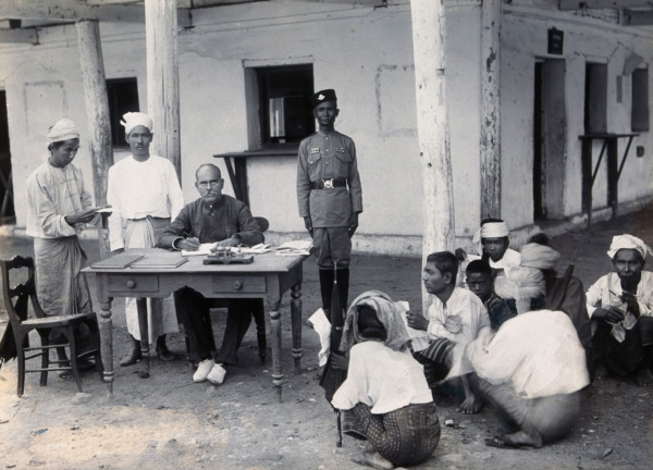 A man sitting at a table examining passports, during a plague epidemic in Mandalay, 1906. Creator: Unknown.