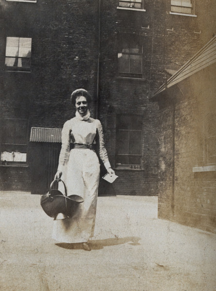 St Bartholomew's Hospital, London: a smiling nurse carrying a coal scuttle, c1890. Creator: Unknown.
