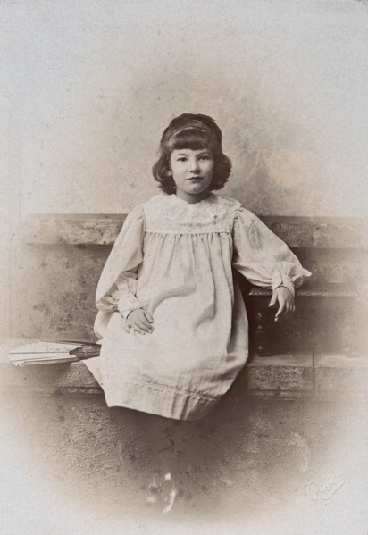 A girl, sitting on a stone bench with a fan folded at her side, c1890s. Creator: Arthur Reston.