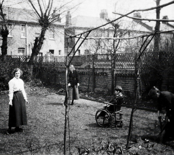 A physically disabled boy sitting in a wheelchair in the back garden of a semi..., c1910/1925. Creator: Unknown.