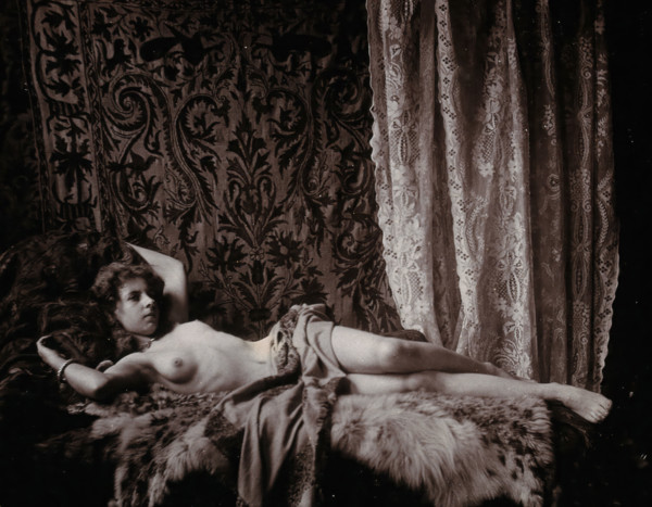 A young woman, posing semi-naked in a photographic studio, lying full-length on a fur..., c1900. Creator: Unknown.