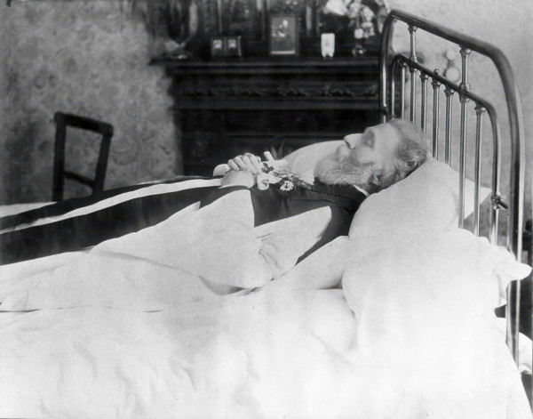 A dead man, wearing robes, lying on his deathbed, (1900?). Creator: Unknown.