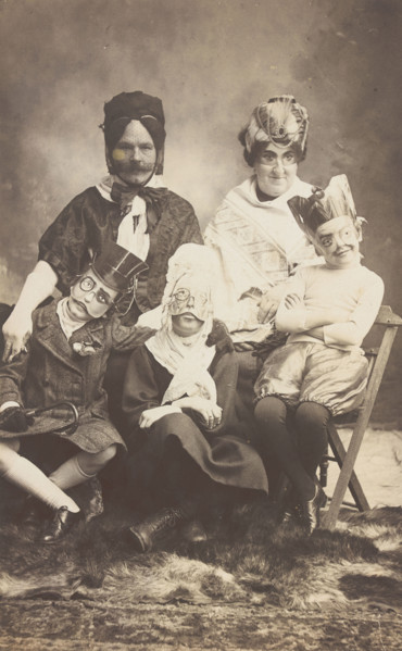A family, all members wearing grotesque masks, the father in drag, c1910. Creator: Unknown.