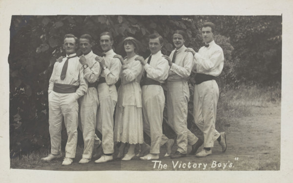Entertainers, one in drag, pose in a line in front of foliage, [between 1910 and 1919?]. Creator: Unknown.