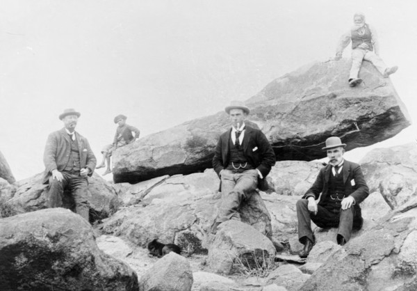 Unknown men and boy, unknown location posing on large rocks, c1900s. Creator: Robert Augustus Henry L'Estrange.