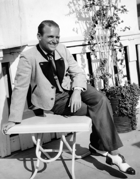 Douglas FAIRBANKS Jr., seated on a table
