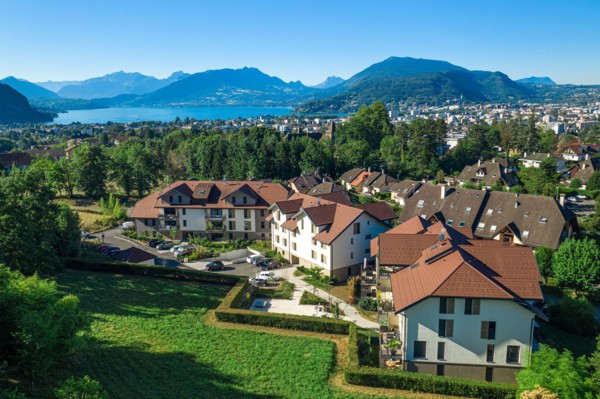 Complex of houses with mountains and large lake in distance. Aerial view of residential real estate in Annecy, France