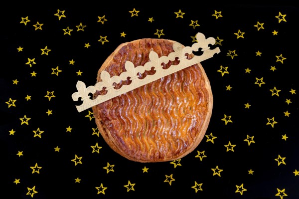 Galette des rois, french kingcake with a golden crown on a black slate background with golden star-studded