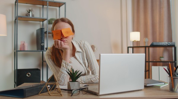 Tired woman teacher using laptop computer with funny stickers on eyes sleeps at workplace, napping