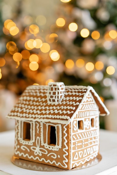 Gingerbread house on table. Defocused lights of Christmas tree. Morning in the bright living room. Holiday mood.