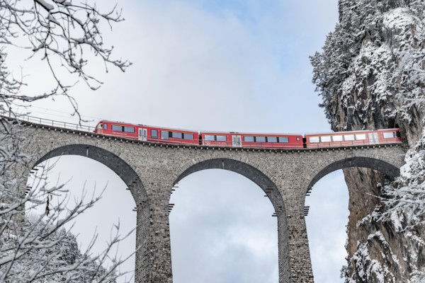 The Landwasser Viaduct with famous train of red color at winter time, landmark of Switzerland, snowing, Glacier express