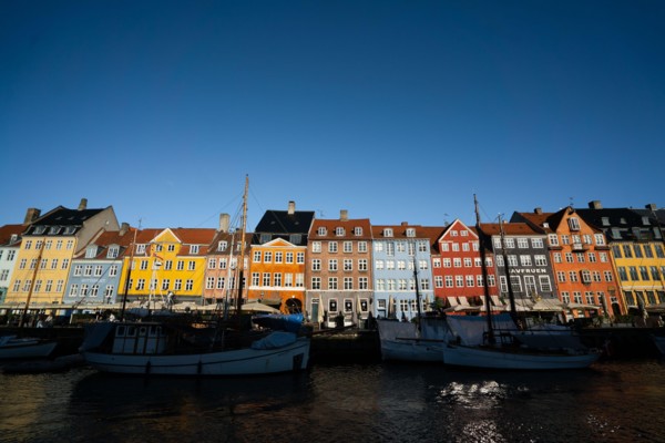The colourful streets of Copenhagen, Denmark, along Nyhavn Quayside, on a sunny day with a blue sky.
