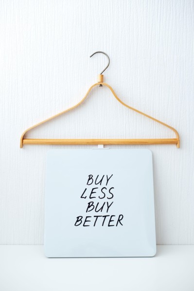 Sustainable consumption and production. Circular economy, Sustainable fashion concept with wooden clothes hangers and text Buy less, buy better