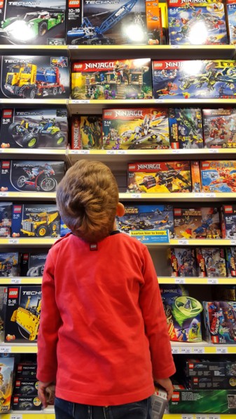 little boy admiring a plaything-shelf with LEGO packings