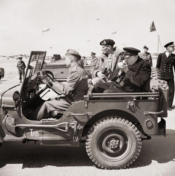 Winston Churchill lights a cigar in the back of a jeep while touring the Normandy beaches with General Mongomery, 12 June 1944.