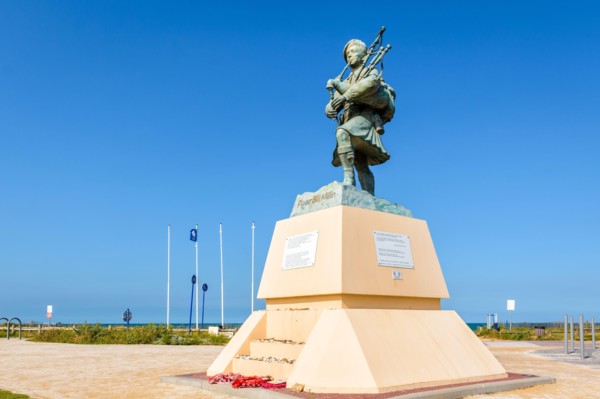 Statue to WWII British commando and piper Bill Millin playing the pipes in kilt, by sculptor Gaetan Ader, erected on Sword beach, Normandy, in 2013.