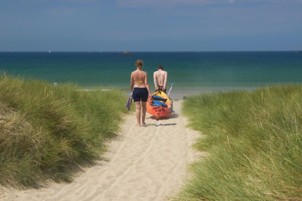 France, Quiberon couple dragging kayak through sand dune towards the sea
