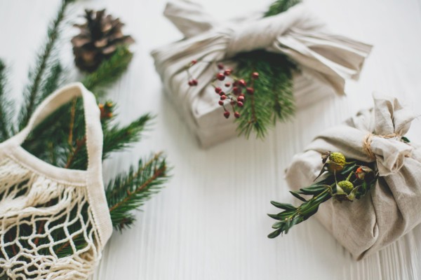 Stylish christmas gifts wrapped in linen fabric with green branch and reusable shopping bag with green spruce on rustic wooden background. Zero waste