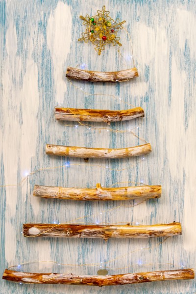 An original alternative to the Christmas tree made of wooden branches, decorated with a garland on a blue-white background.