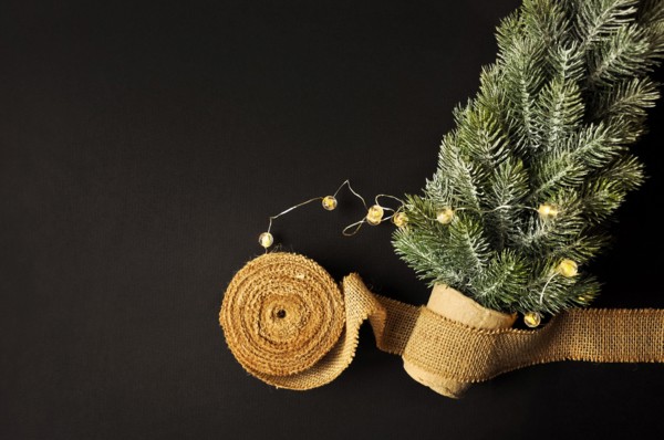 Preparation of decorations for winter celebrations. Artificial Christmas tree, natural jute fiber strip, dark background, cozy lighting