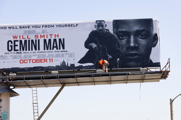 Huge billboard for the film Gemini, starring Will Smith, being erected by a man in orange hi viz jacket above the street. Los Angeles, California, USA