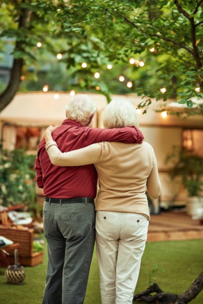 Back view of senior married couple looking at their campervan and hugging while standing outdoors. Travel concept