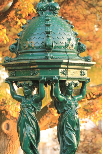 Wallace fountain in Paris by fall / One of the drinking fountains in Paris so called "Wallace fountains" in autumn with yellow foliage as a background