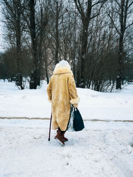Winter. Back view of elderly women in fur coat with bags walking along snow with cane. Seniors, lifestyle concept